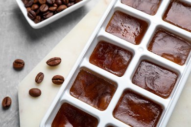 Photo of Ice cubes in tray and coffee beans on grey table, closeup