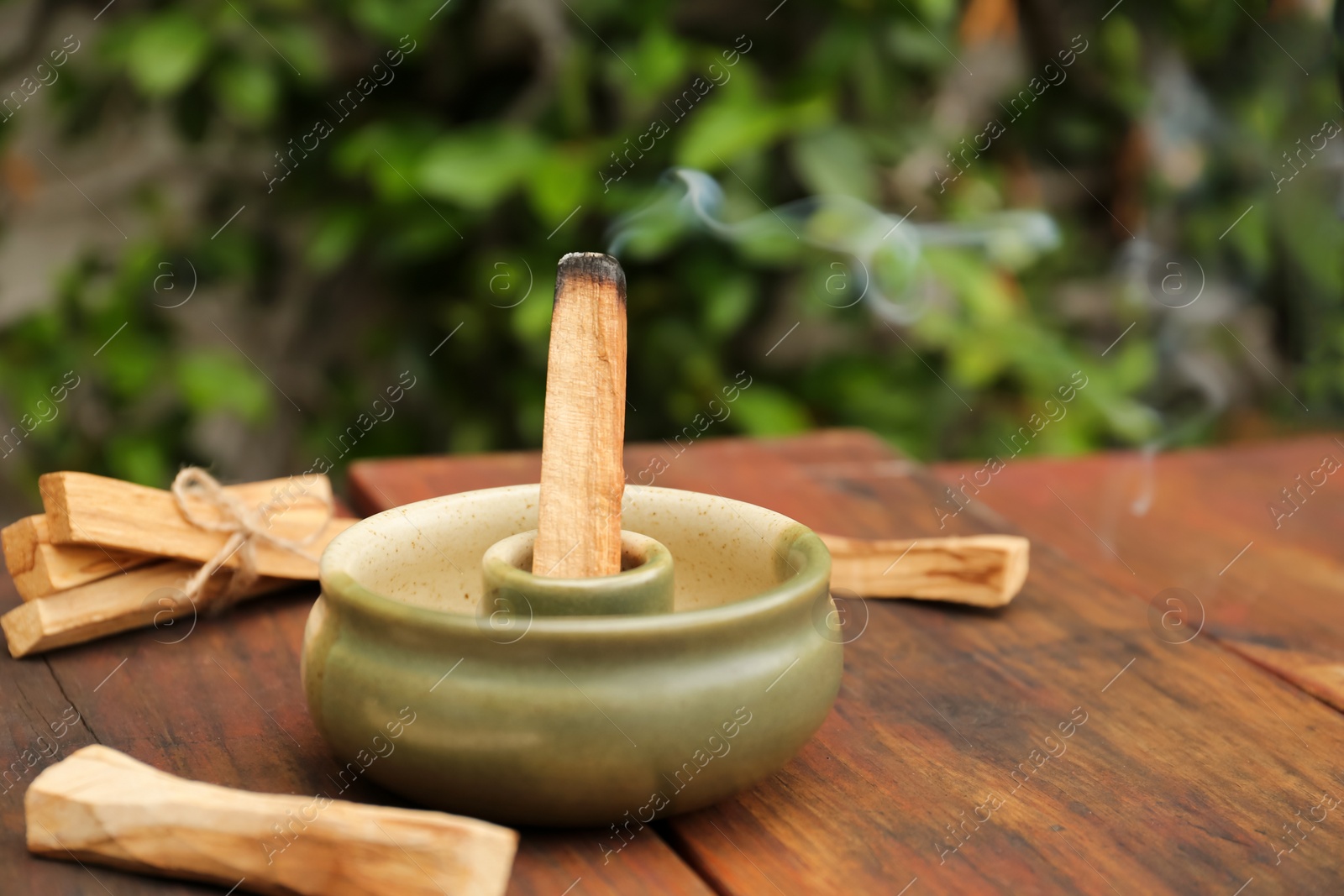 Photo of Palo Santo stick smoldering in holder on wooden table outdoors