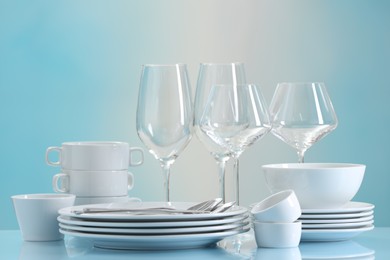 Photo of Set of many clean dishware, cutlery and glasses on light blue table