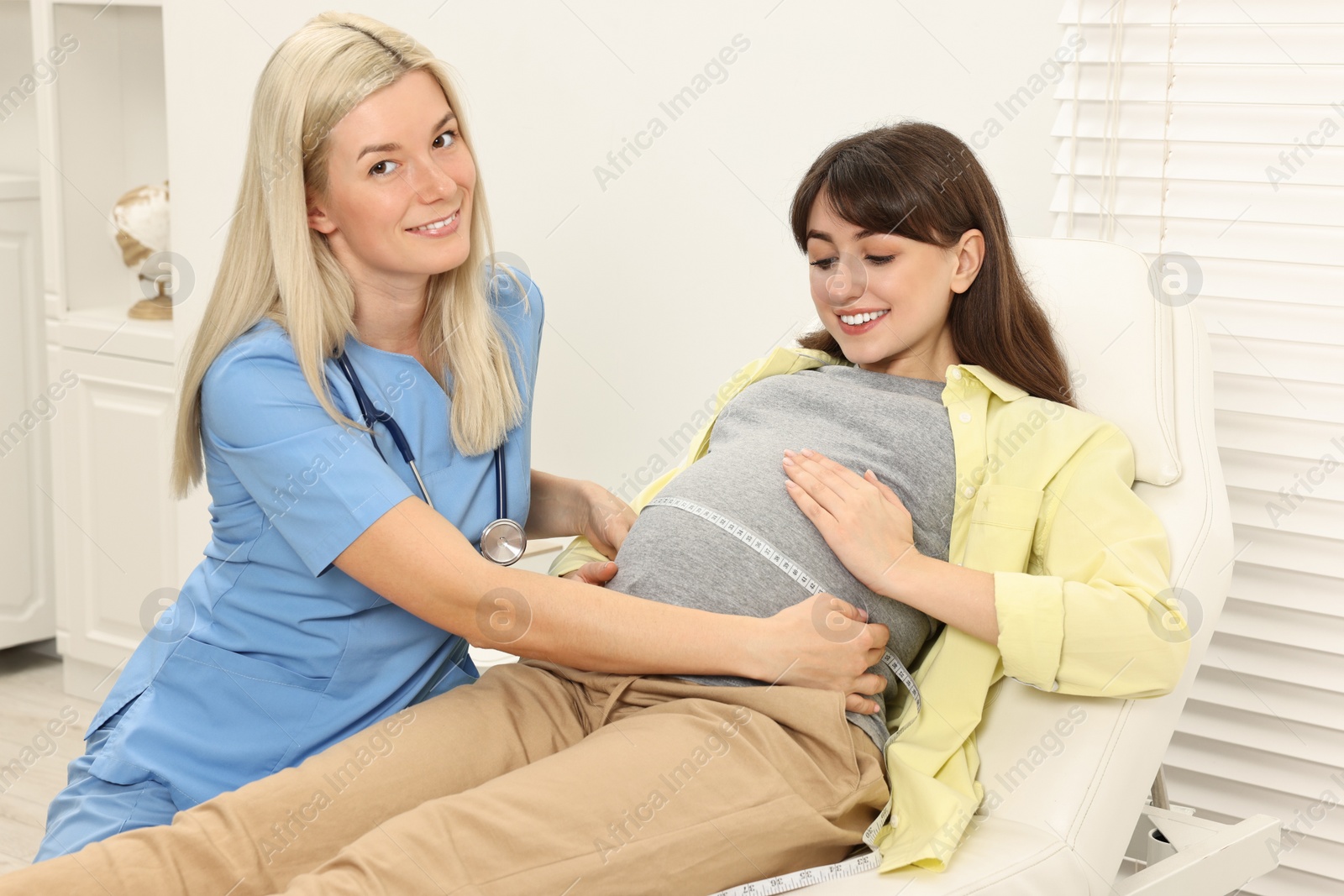 Photo of Pregnancy checkup. Smiling doctor measuring patient's tummy in clinic