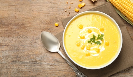 Photo of Delicious creamy corn soup served on wooden table, flat lay. Space for text