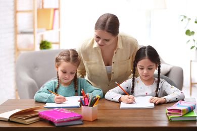 Photo of Mother helping her daughters with homework at table indoors