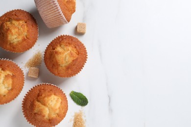 Photo of Delicious sweet muffins and brown sugar on white marble table, flat lay. Space for text