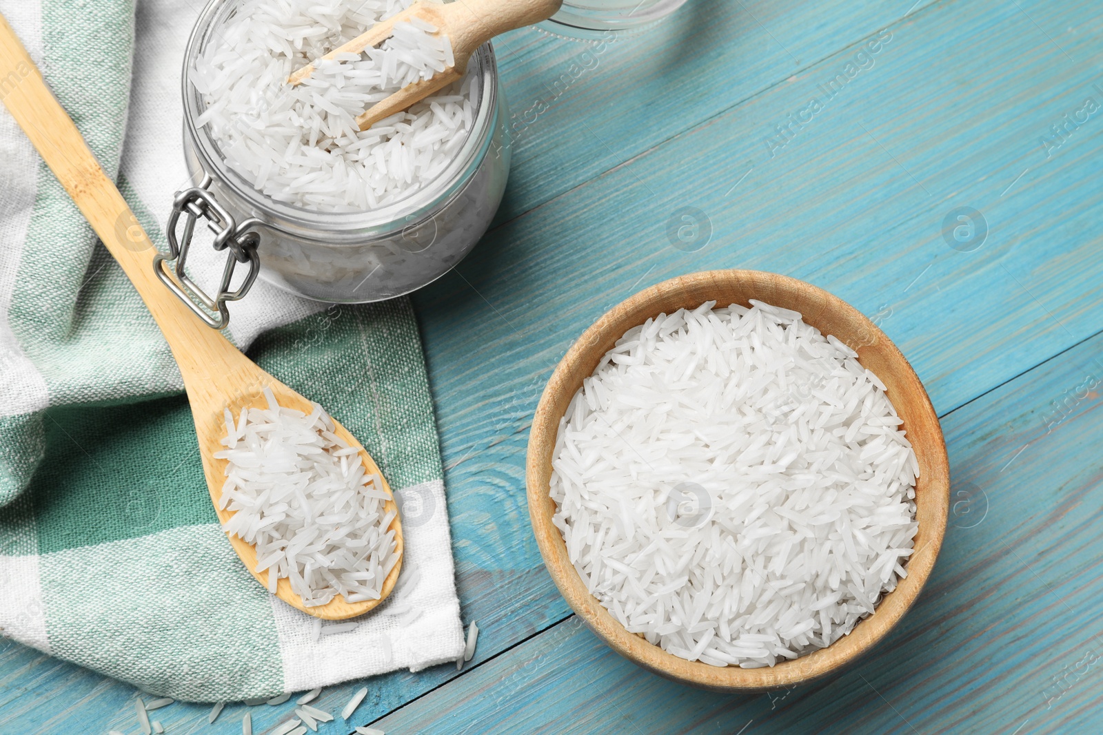 Photo of Raw basmati rice in bowl, jar, spoon and scoop on light blue wooden table, flat lay