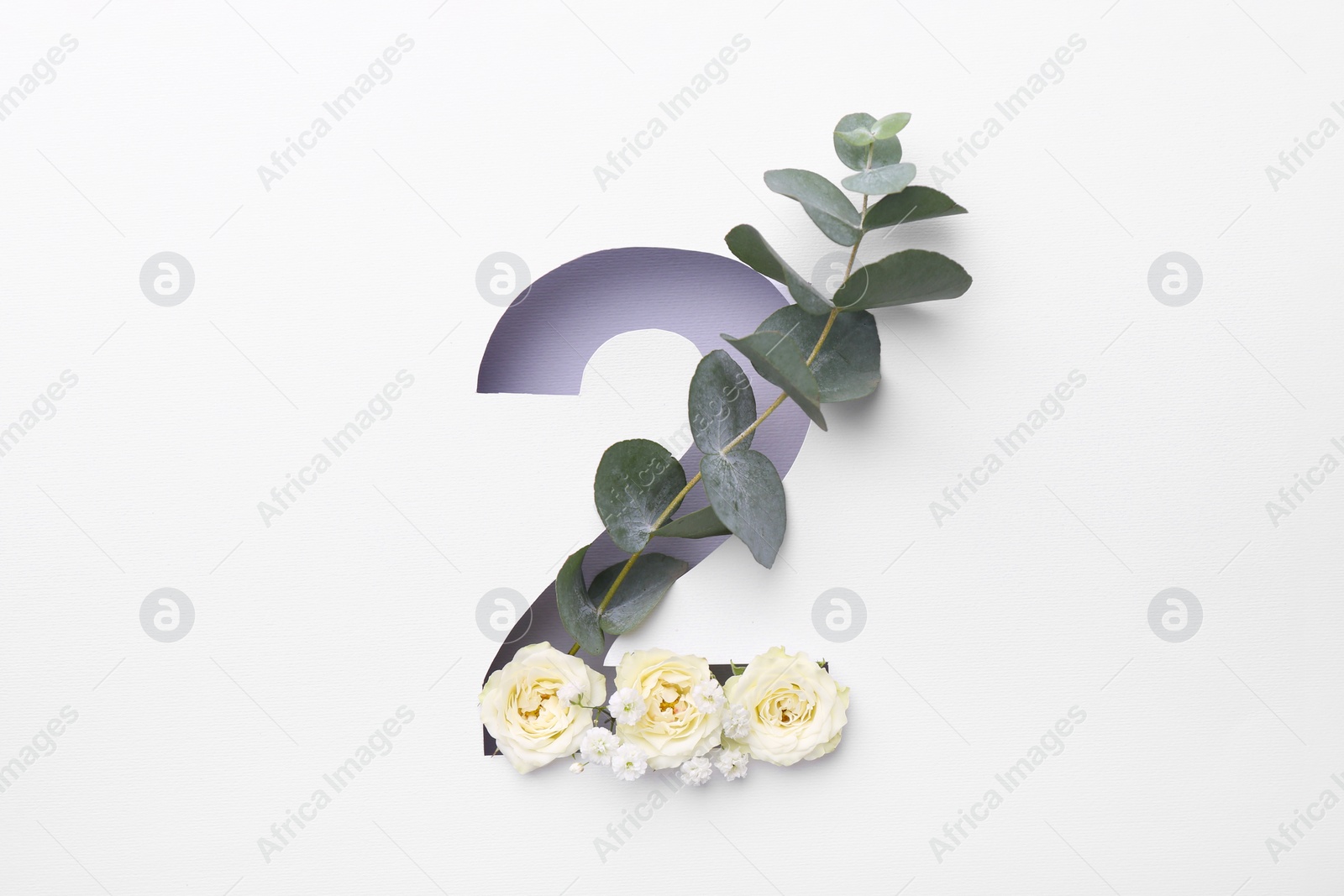 Photo of Number 2 shape hole in white paper with beautiful flowers and eucalyptus branch, top view