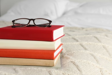 Photo of Books and glasses on white soft blanket in bedroom, space for text