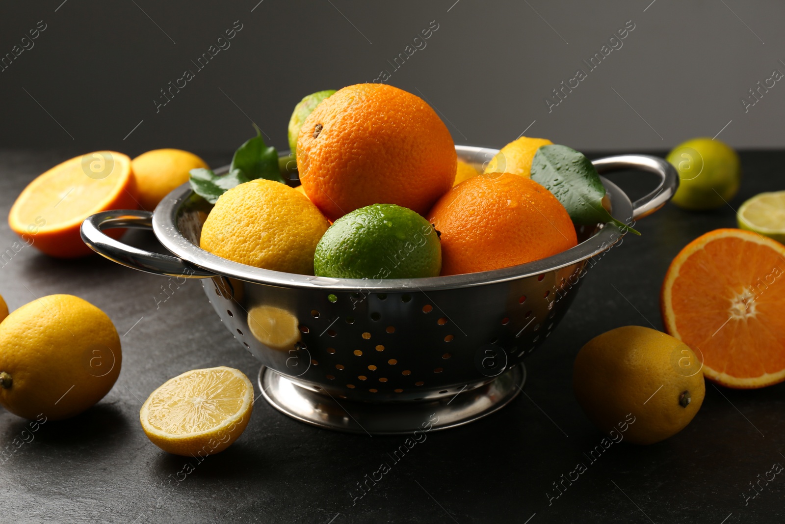 Photo of Fresh citrus fruits in colander on dark table, closeup