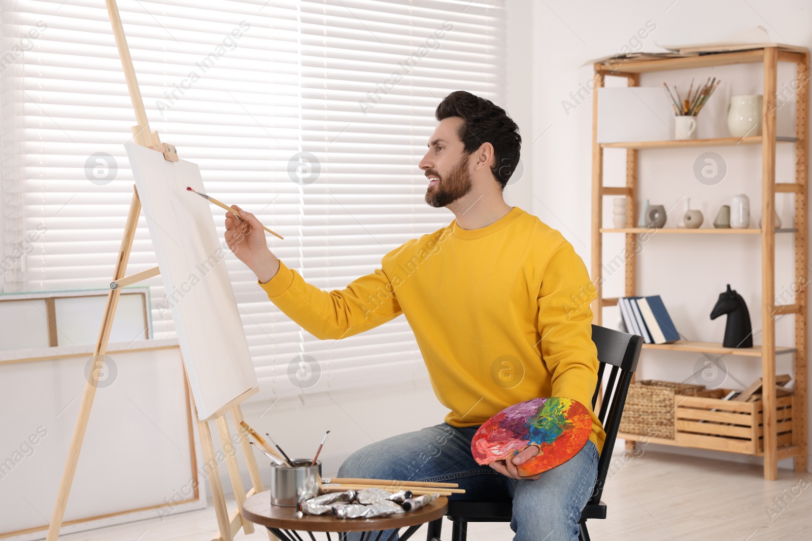 Photo of Man painting in studio. Using easel to hold canvas