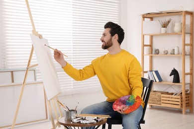 Man painting in studio. Using easel to hold canvas