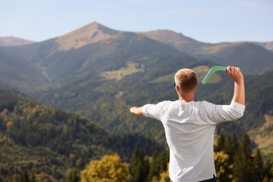 Photo of Man throwing boomerang in mountains on sunny day, back view. Space for text