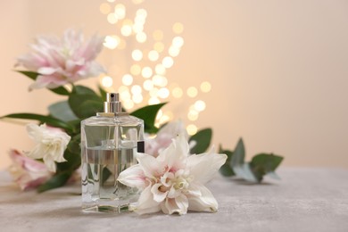 Bottle of perfume and beautiful lily flowers on table against beige background with blurred lights, space for text