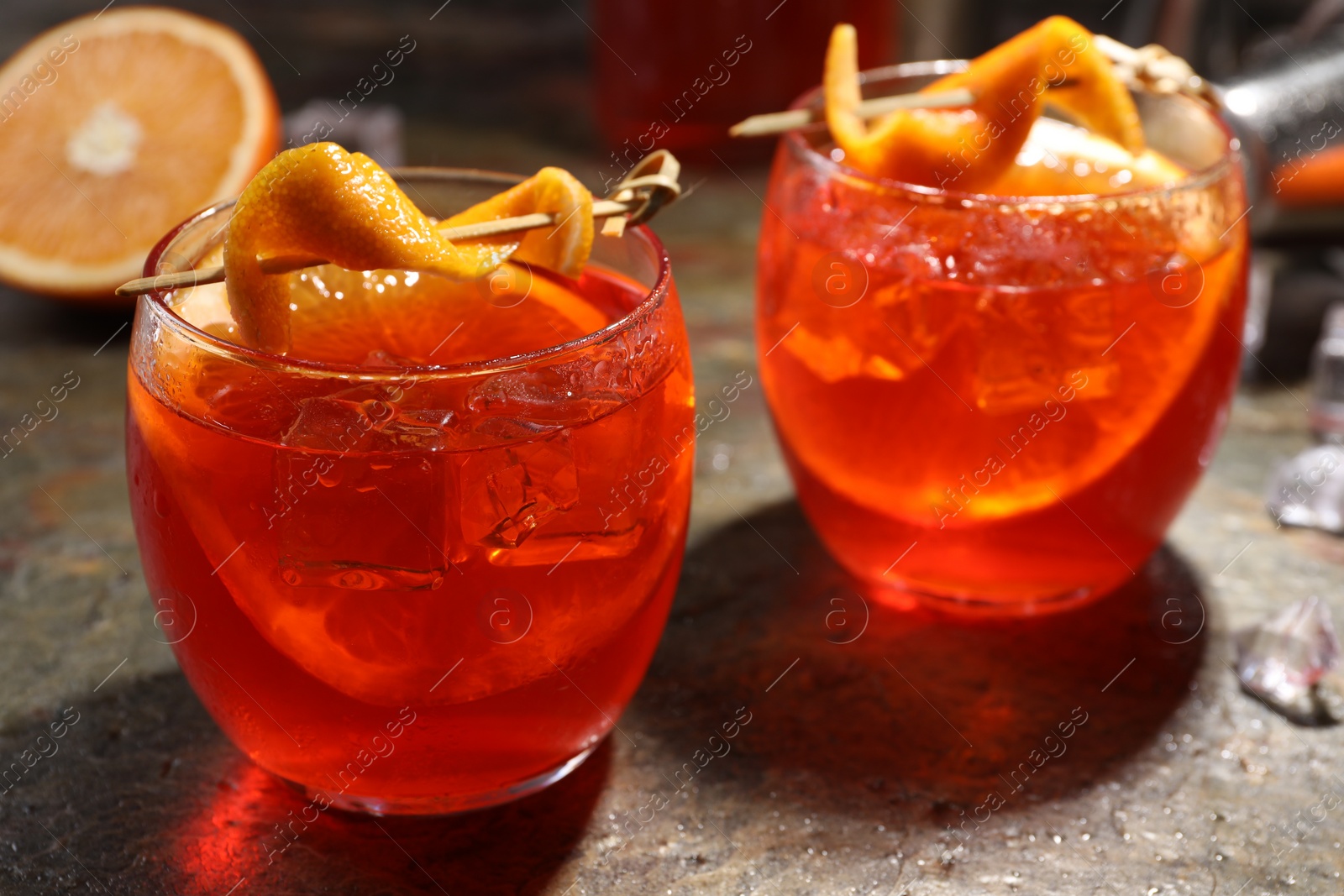 Photo of Aperol spritz cocktail, ice cubes and orange slices in glasses on grey textured table, closeup