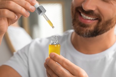 Smiling man with cosmetic serum indoors, closeup