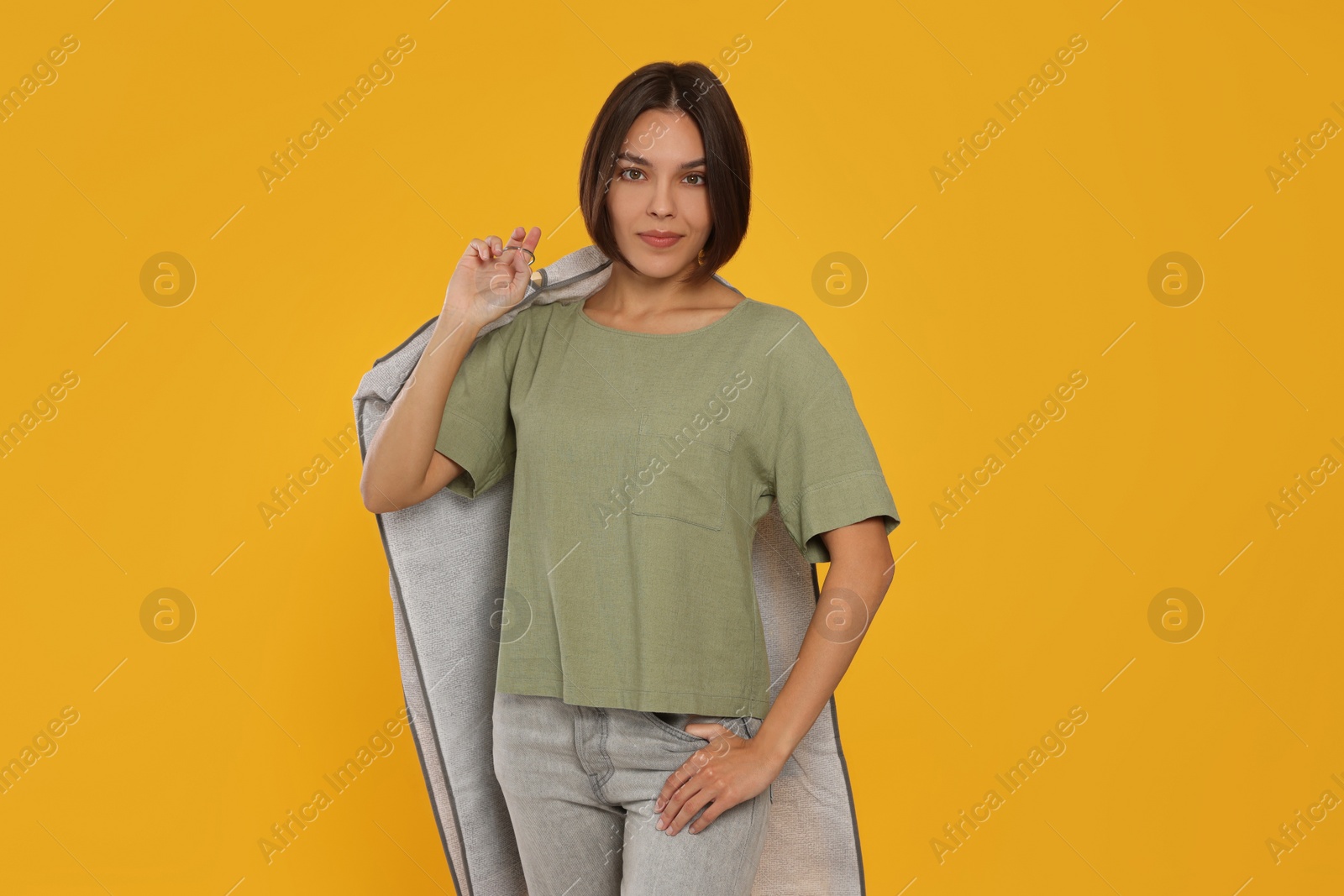 Photo of Woman holding garment cover with clothes on yellow background. Dry-cleaning service