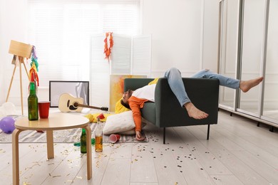 Photo of Young man sleeping on sofa in messy room after party