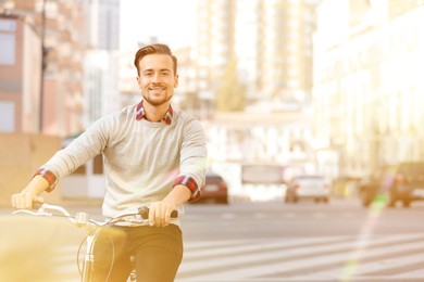 Image of Handsome happy man riding bicycle in city on sunny day