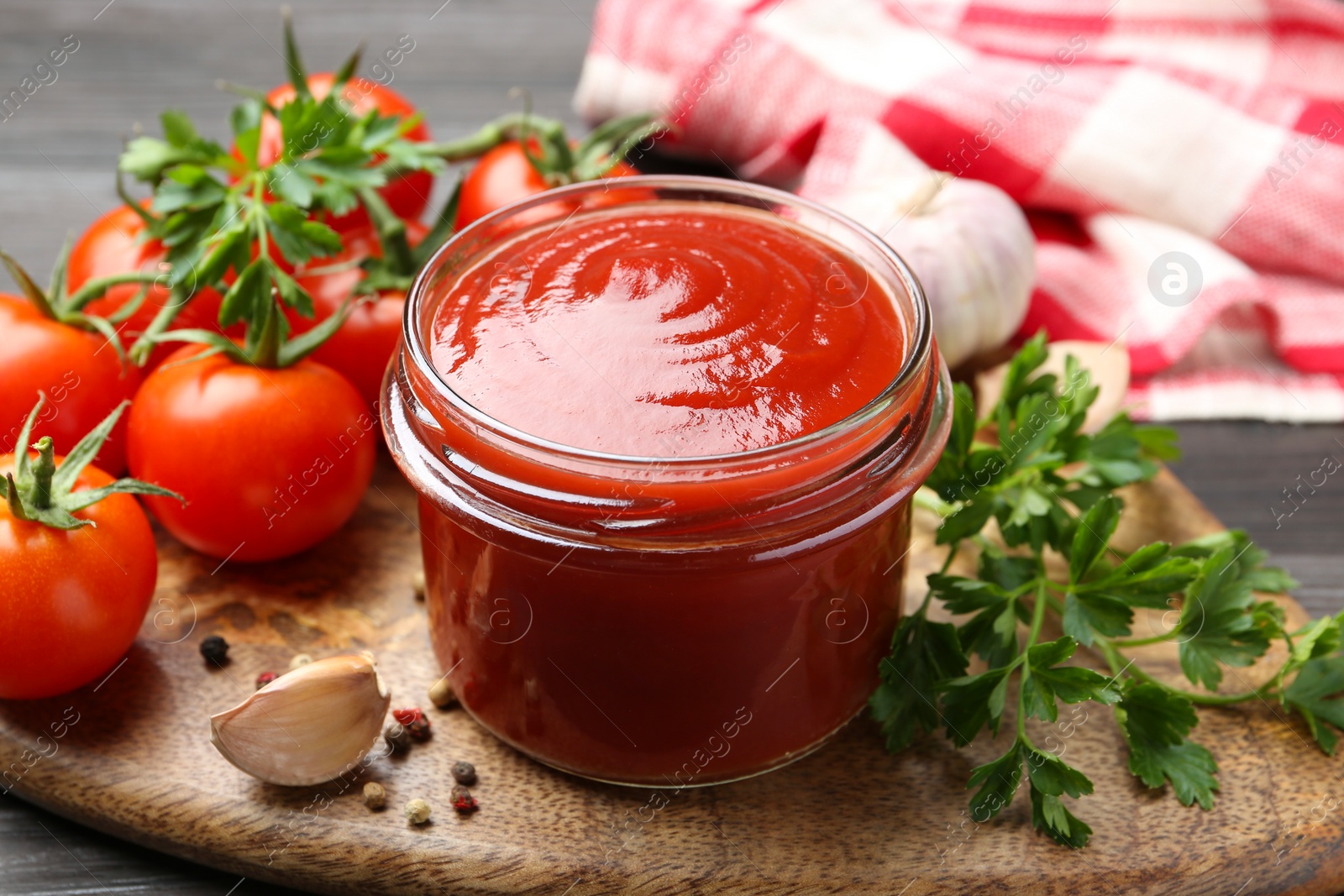 Photo of Tasty ketchup, fresh tomatoes, parsley and spices on grey wooden table