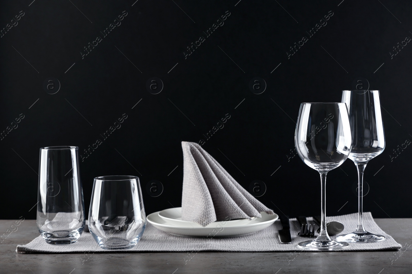 Photo of Table setting with empty glasses, plates and cutlery on table against black background