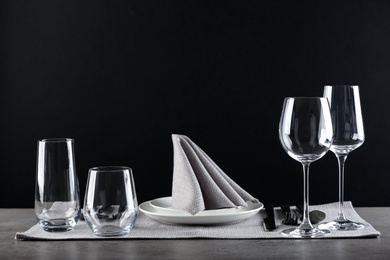 Table setting with empty glasses, plates and cutlery on table against black background