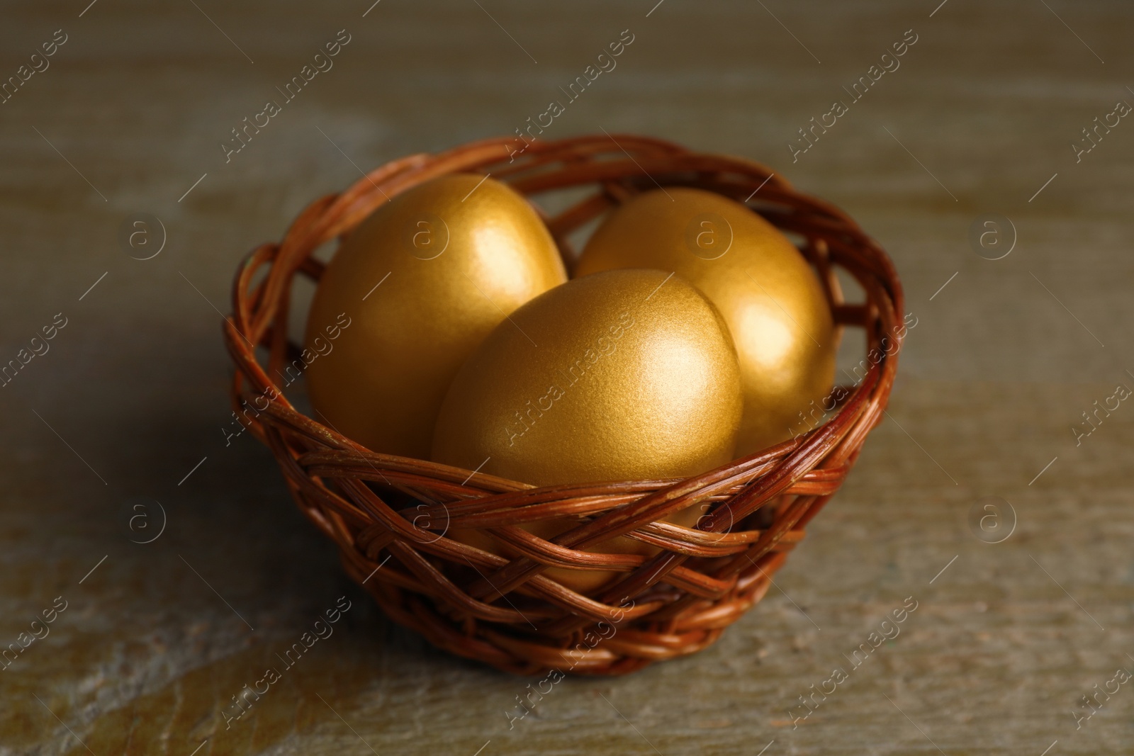 Photo of Wicker basket with golden eggs on wooden table, closeup