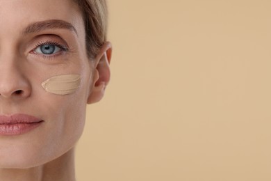 Photo of Woman with swatch of foundation on face against beige background, closeup. Space for text
