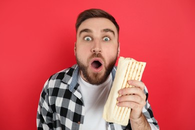 Photo of Emotional young man with delicious shawarma on red background