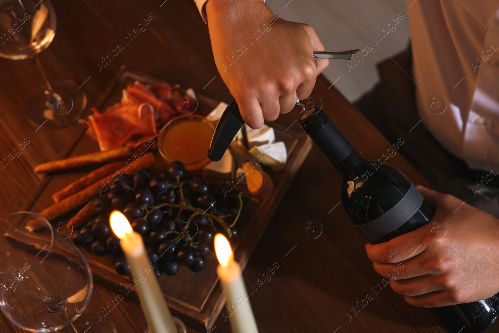 Photo of Romantic dinner. Man opening wine bottle with corkscrew at table indoors, above view