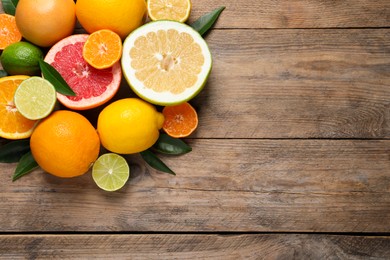 Photo of Different ripe citrus fruits with green leaves on wooden table, flat lay. Space for text