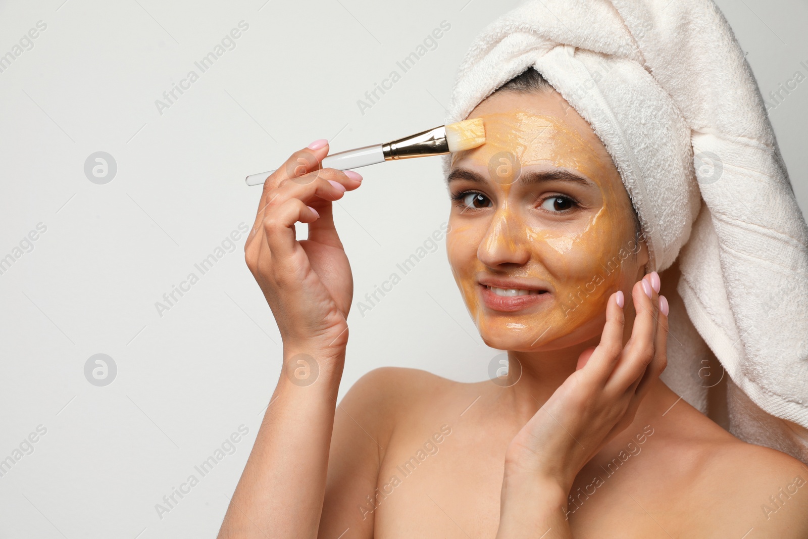 Photo of Beautiful woman applying mask onto face against light background