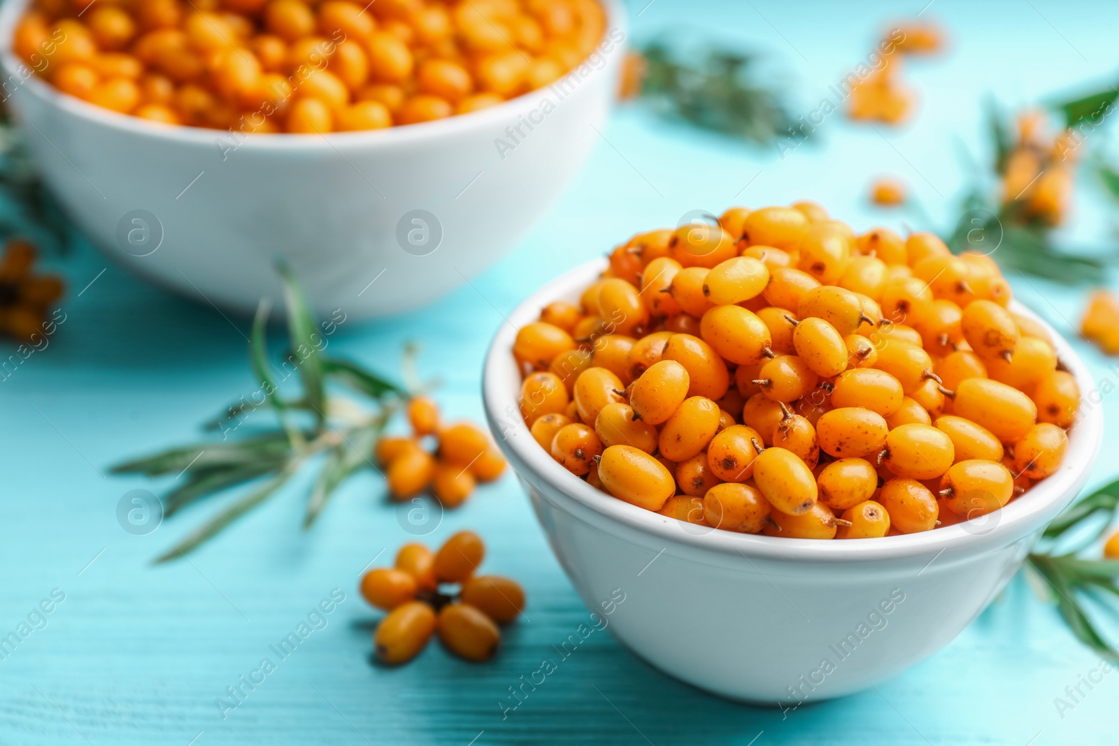 Photo of Fresh ripe sea buckthorn in bowl on light blue wooden table, closeup