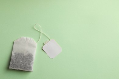 Photo of Paper tea bag with tag on light green background, top view. Space for text