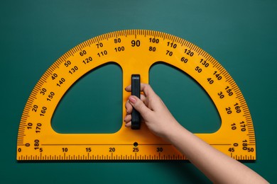 Photo of Woman holding protractor with measuring length and degrees markings near green board, closeup