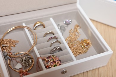 Jewelry box with stylish bracelets and other accessories on wooden table, closeup