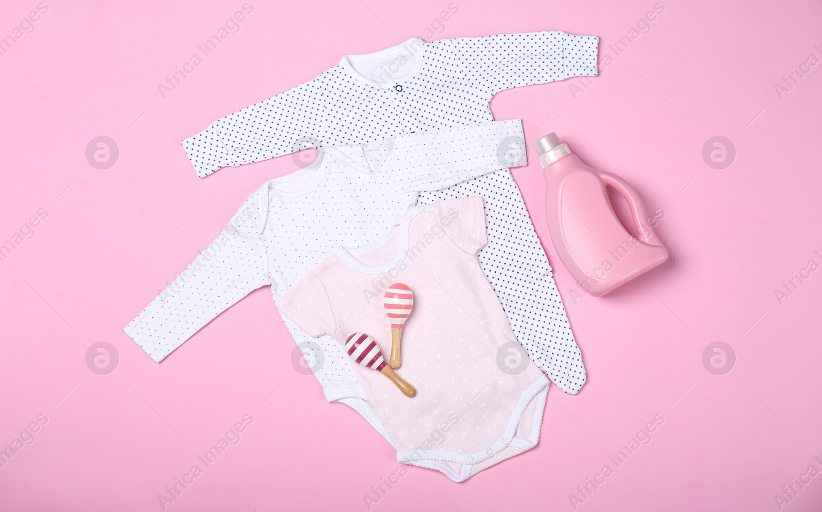 Photo of Flat lay composition with bottle of detergent and children's clothes on pink background