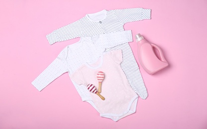 Photo of Flat lay composition with bottle of detergent and children's clothes on pink background