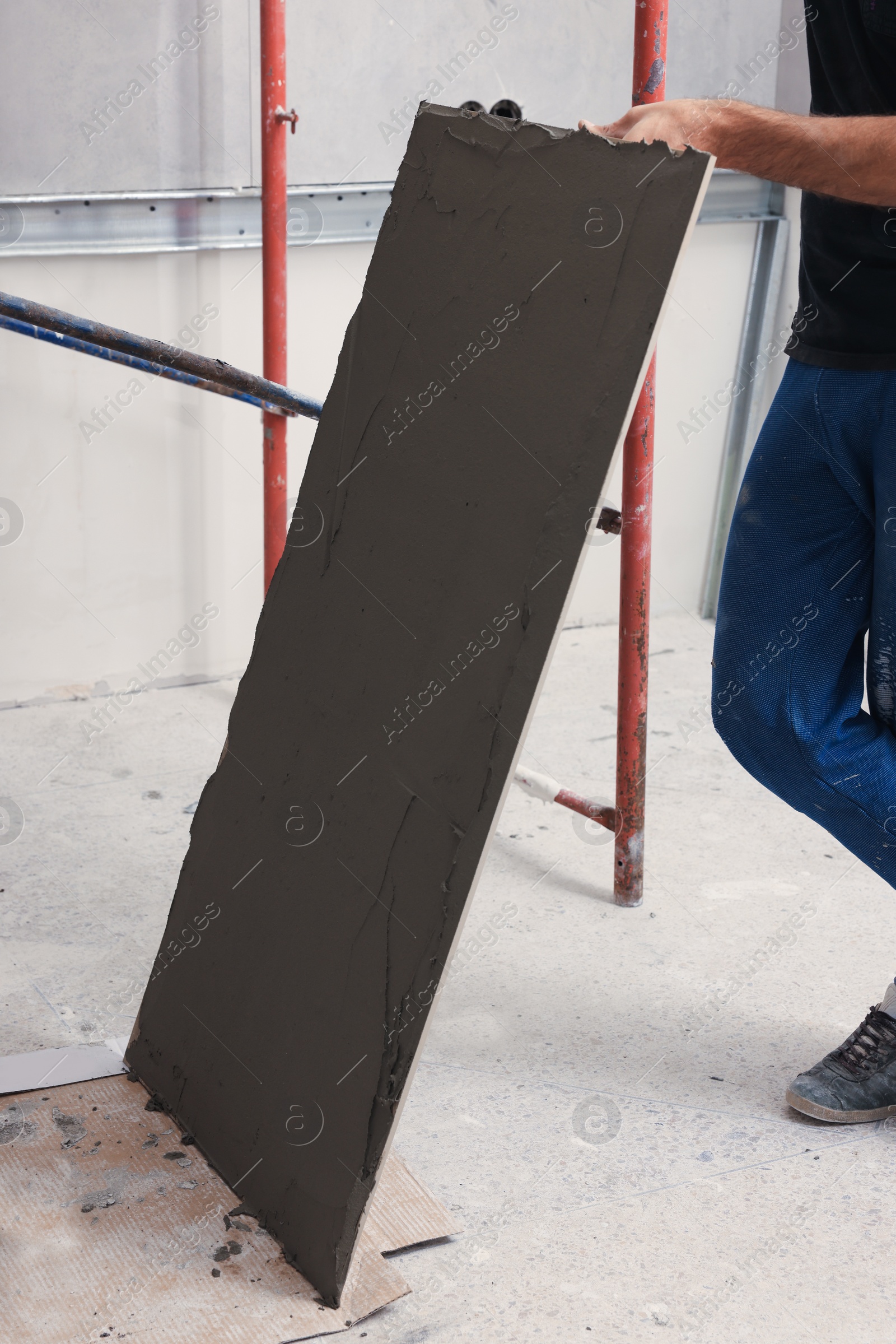 Photo of Worker holding tile with adhesive mix indoors, closeup