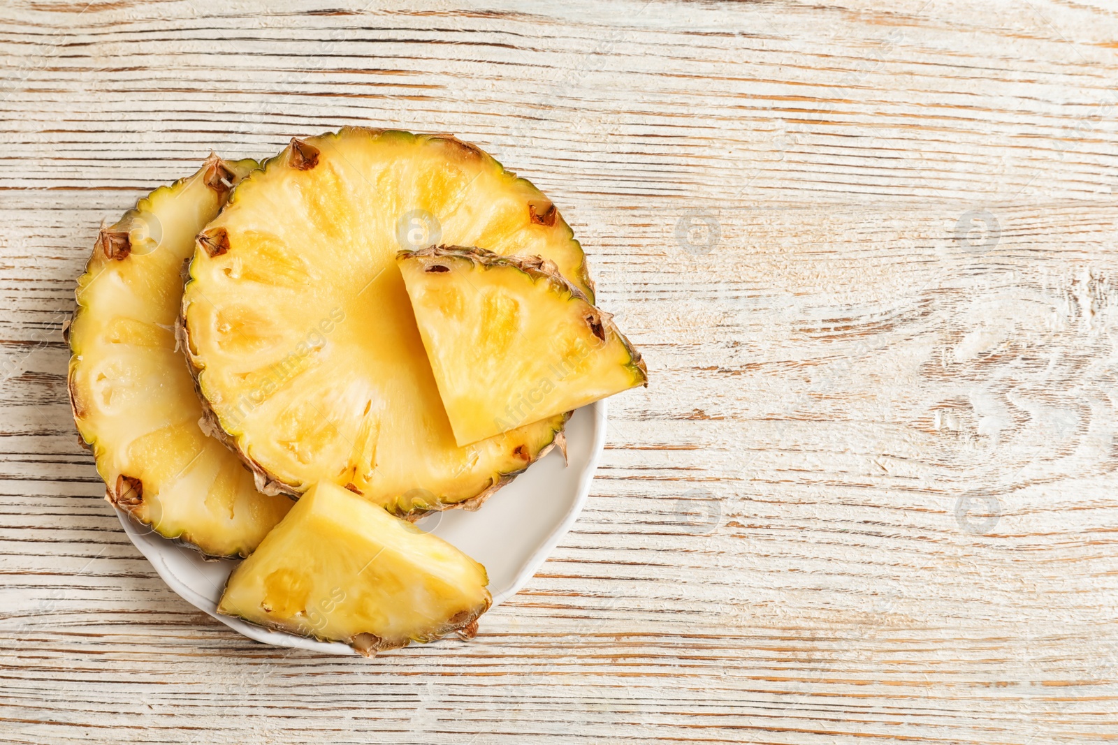 Photo of Plate with fresh pineapple slices on wooden background