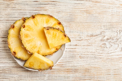 Plate with fresh pineapple slices on wooden background