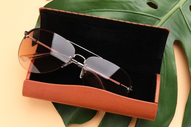 Photo of Stylish sunglasses in brown leather case on beige background, above view