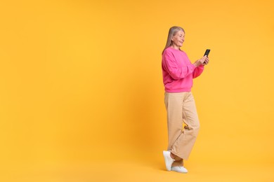 Senior woman with phone on orange background, space for text