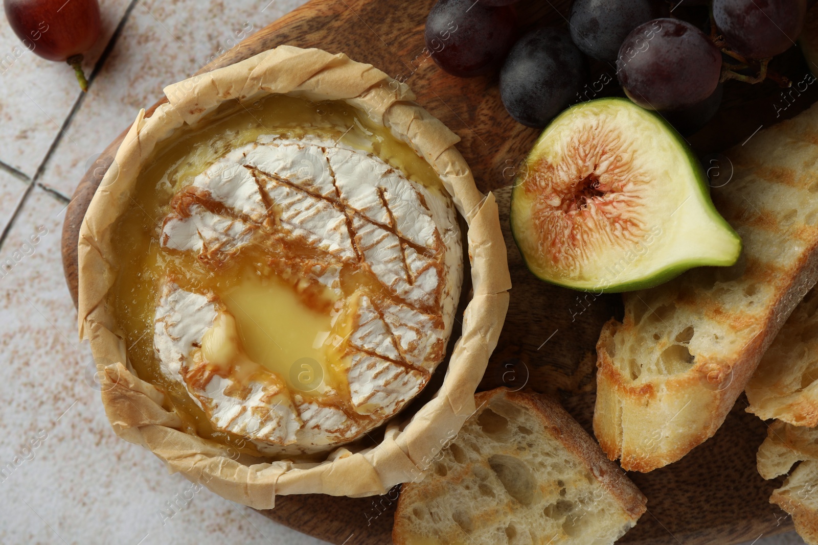 Photo of Tasty baked brie cheese and products on light tiled table, flat lay