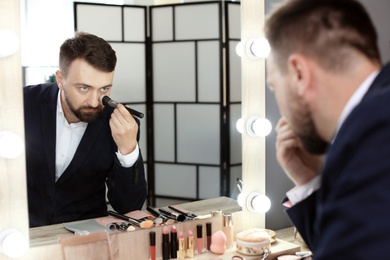 Young man using makeup brush near mirror in dressing room