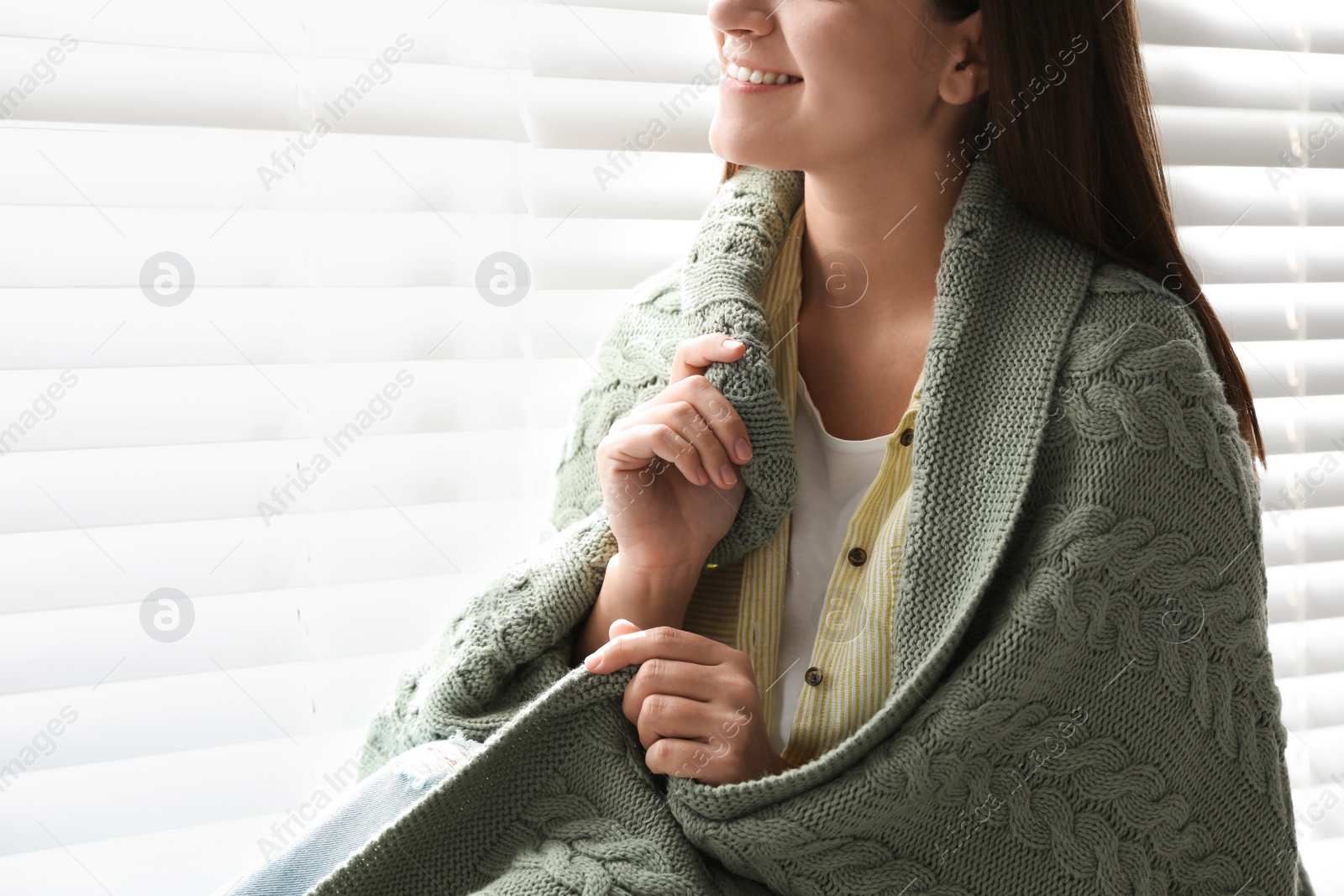 Photo of Woman covered with warm green plaid sitting near window indoors, closeup