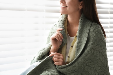 Photo of Woman covered with warm green plaid sitting near window indoors, closeup