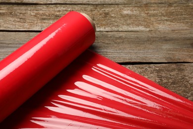 Photo of Roll of red plastic stretch wrap on wooden background, closeup