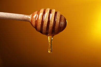 Photo of Pouring honey from dipper against golden background, space for text