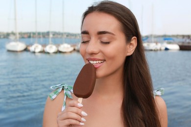 Photo of Beautiful young woman eating ice cream glazed in chocolate near river