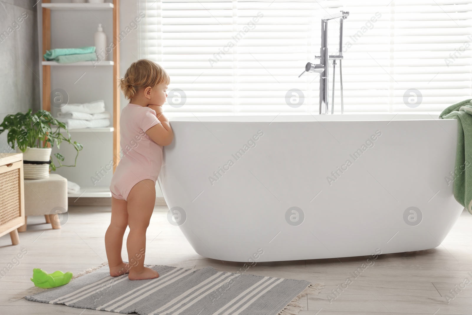 Photo of Cute little girl near tub in bathroom