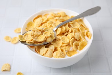 Photo of Breakfast cereal. Tasty corn flakes with milk in bowl and spoon on white tiled table, closeup