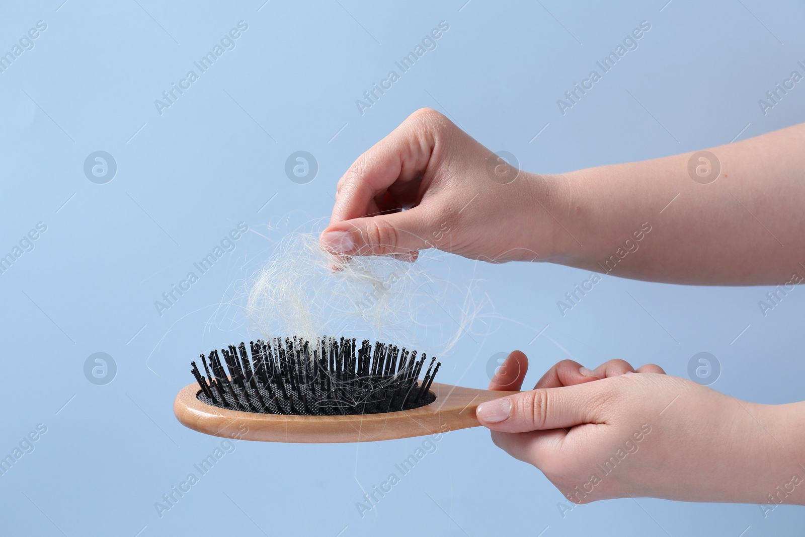 Photo of Woman taking her lost hair from brush on light blue background, closeup